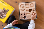 Cuboro standard 50 piece wooden marble run set in it's box, a child's hand can be seen taking a piece out of the box. 