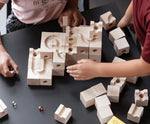 Cuboro standard 50 piece wooden marble run set up on a table with two children playing, placing coloured glass marbles on the track. 