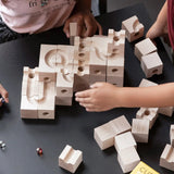 Cuboro standard 50 piece wooden marble run set up on a table with two children playing, placing coloured glass marbles on the track. 