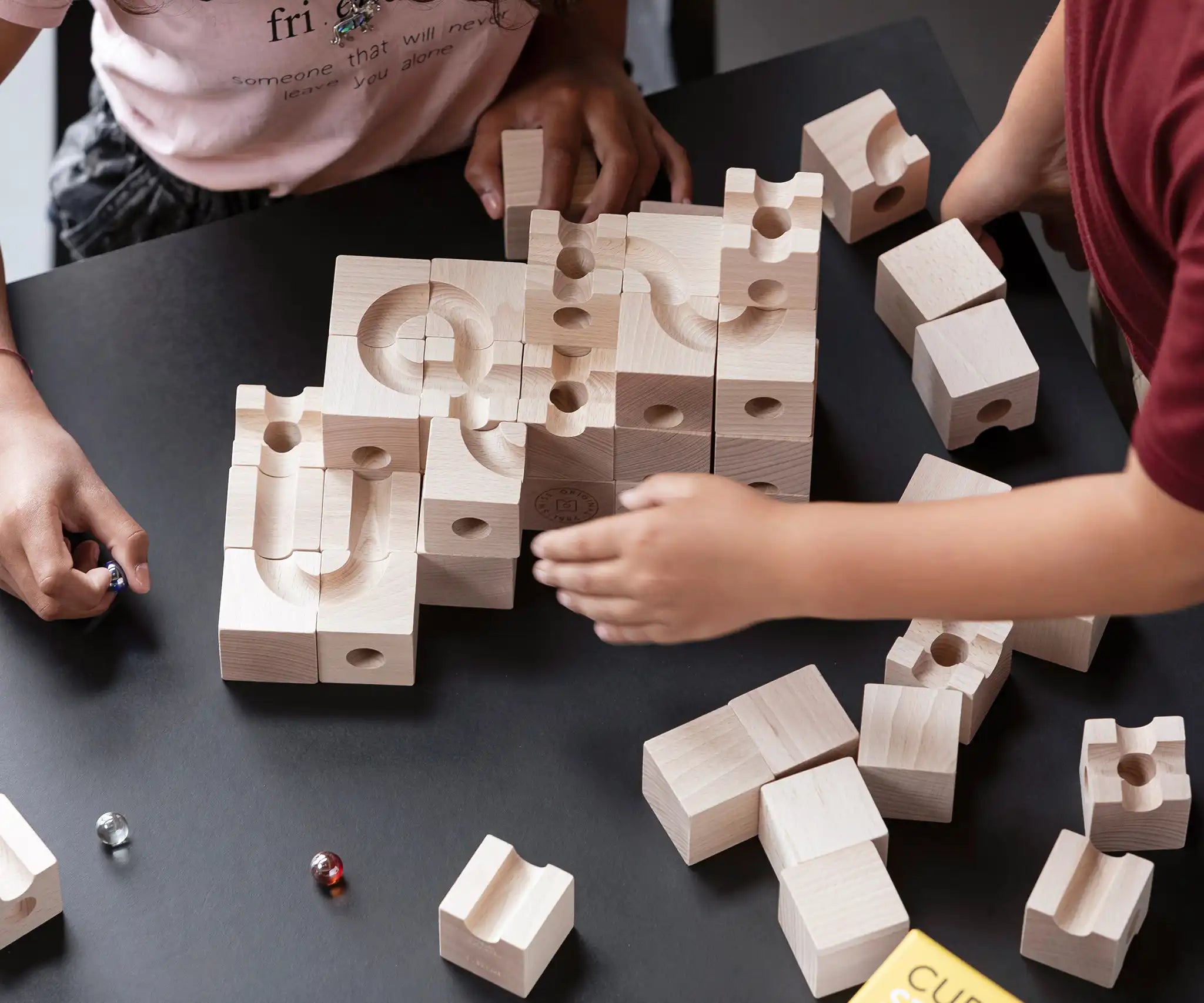 Cuboro standard 50 piece wooden marble run set up on a table with two children playing, placing coloured glass marbles on the track. 