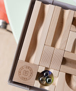 A closeup of the Cuboro WAVE wooden marble run extender set in the box, showing the 'Swiss Original 1986' emblem engraved into one of the wooden pieces