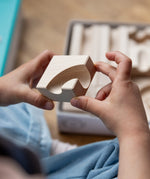 A closeup of a child's hands holding one of the Cuboro WAVE marble run wooden pieces