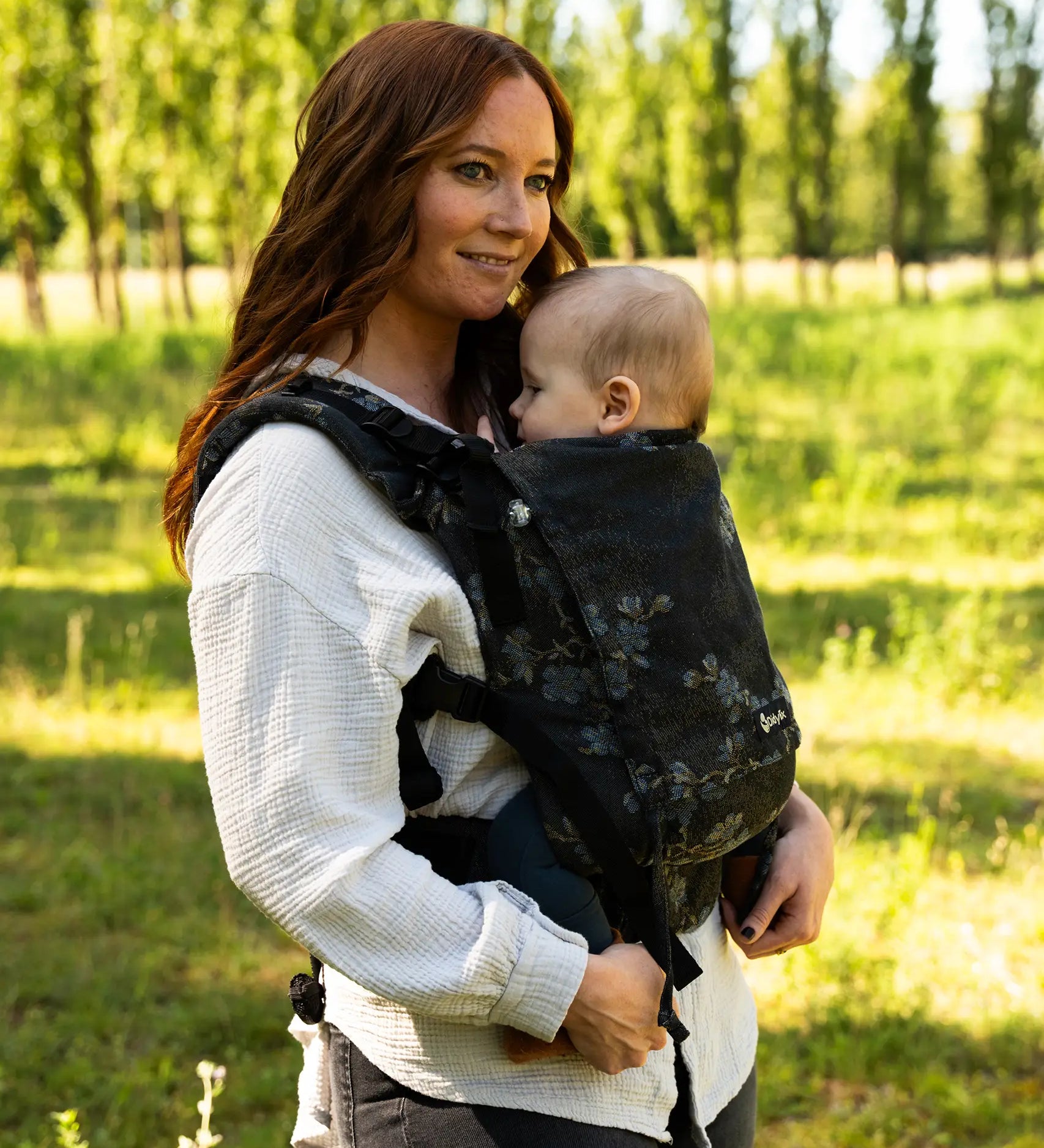 Mother wearing the Didymos didyfix carrier in blue blossom with a baby sitting inside. A soft structured full buckle carrier