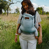 Mother carrying a baby in the Didymos didyfix full buckle, soft structured baby carrier in ocean in the frontal position. 