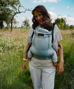 Mother carrying a baby in the Didymos didyfix full buckle, soft structured baby carrier in ocean in the frontal position. 