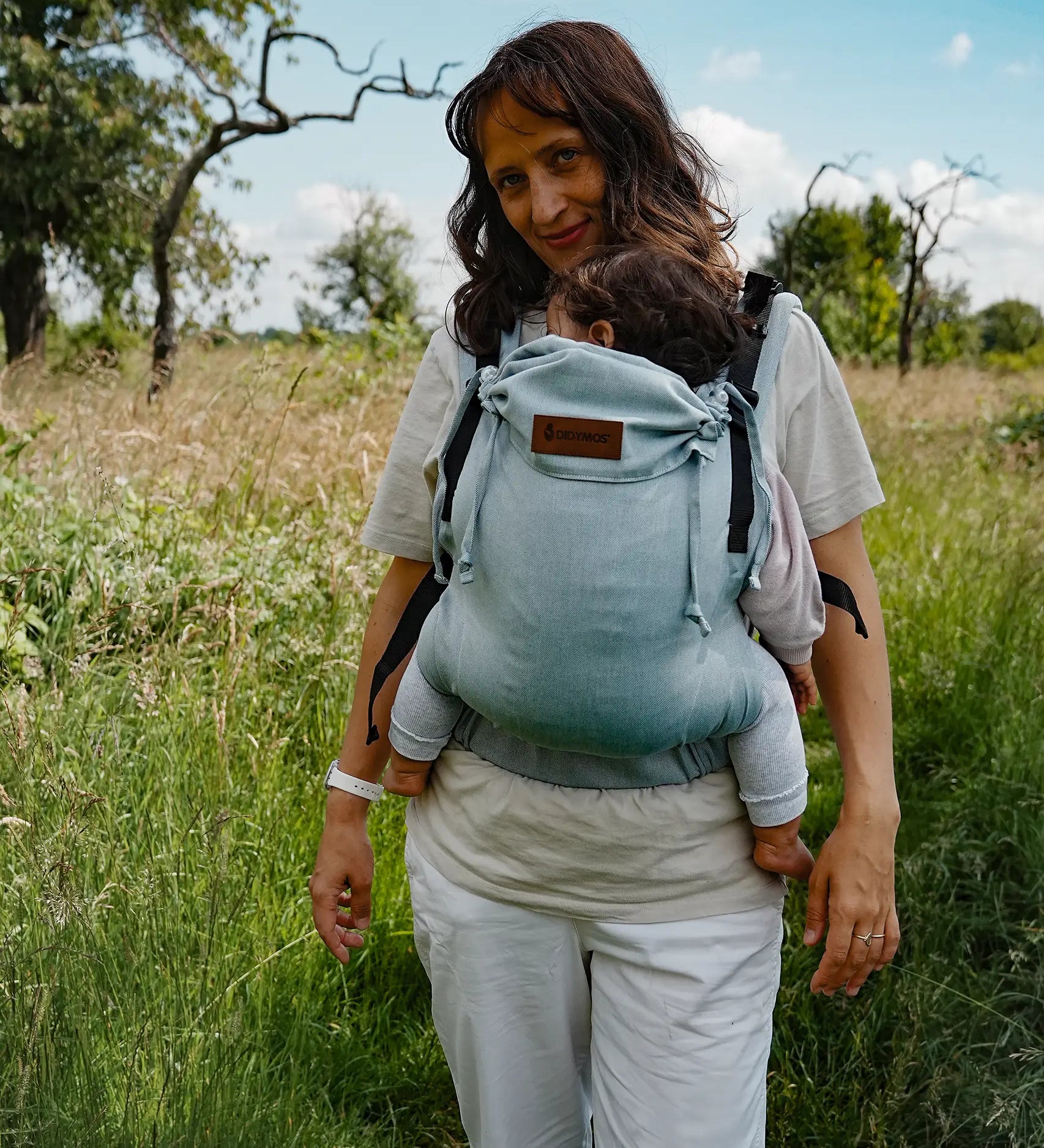 Mother carrying a baby in the Didymos didyfix full buckle, soft structured baby carrier in ocean in the frontal position. 