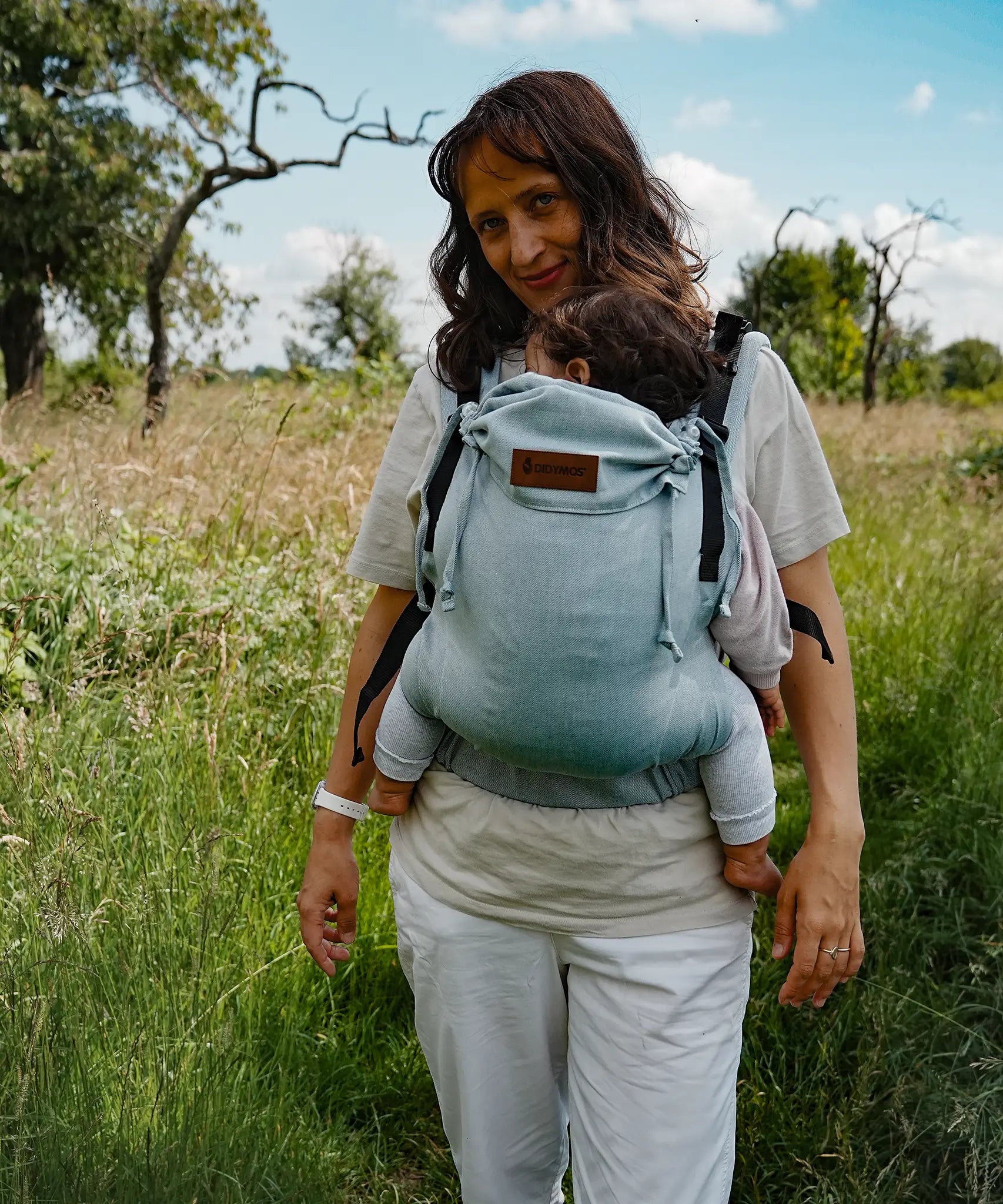 Mother carrying a baby in the Didymos didyfix full buckle, soft structured baby carrier in ocean in the frontal position. 