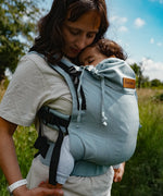 Mother  carrying a baby in a Didymos didyfix full buckle baby carrier in ocean in the frontal position