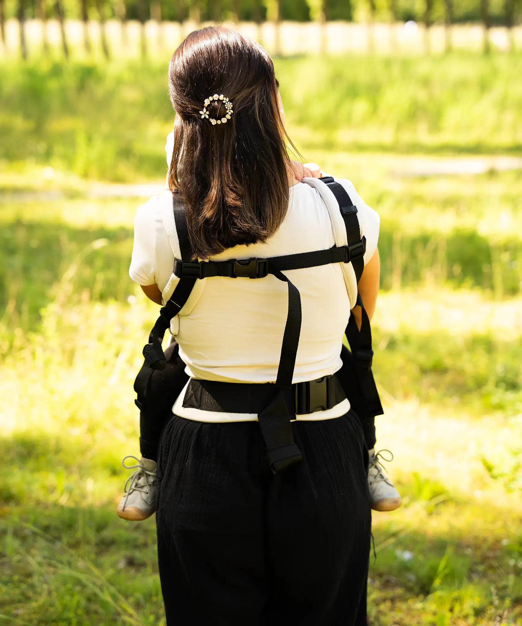 Back of mother wearing a didymos didyfix full buckle baby carrier in the frontal position showing padded shoulders and fastened buckles