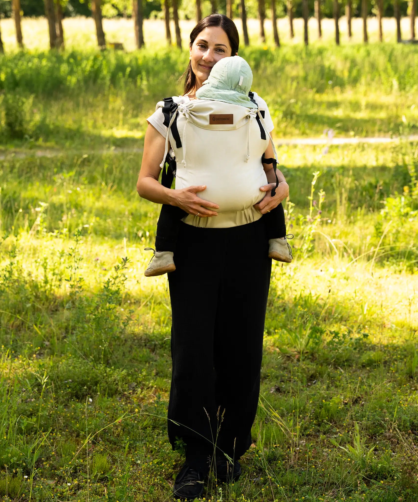 Mother carrying a baby in the frontal position in a Didymos didyfix full buckle soft structured baby carrier in sand colour