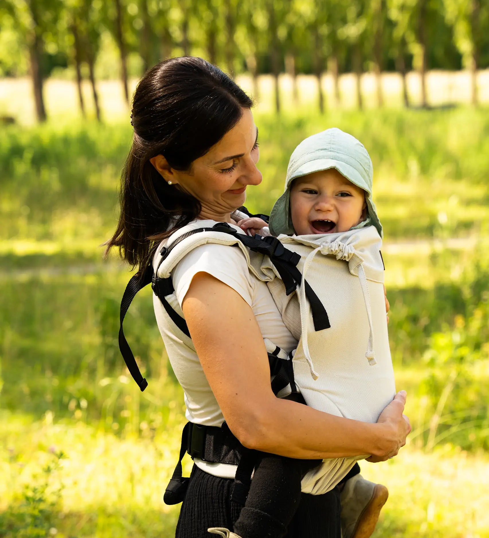 Side of mother carrying a baby in the frontal position in a Didymos didyfix full buckle baby carrier in sand colour showing neck rest supporting baby's head