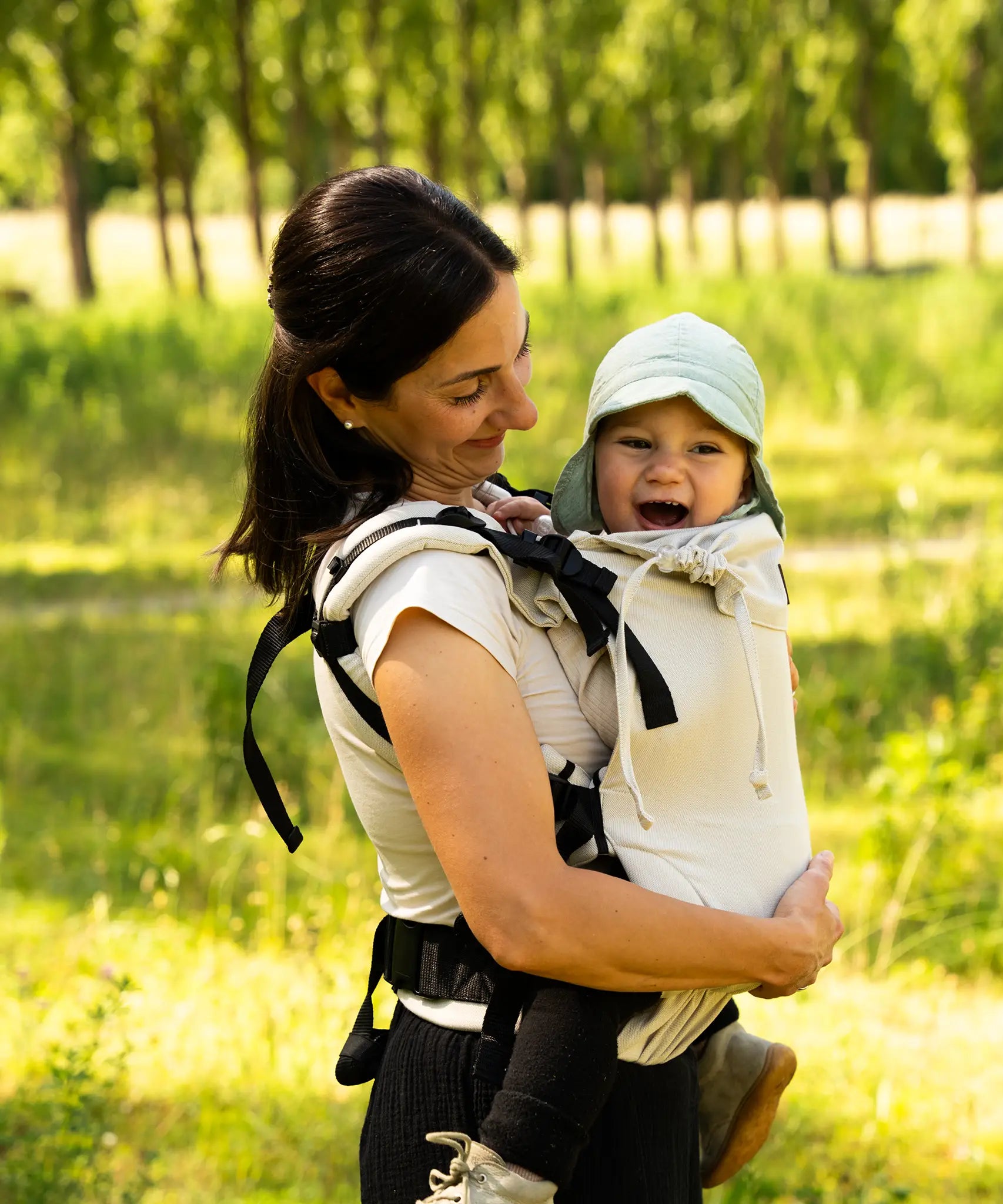 Side of mother carrying a baby in the frontal position in a Didymos didyfix full buckle baby carrier in sand colour showing neck rest supporting baby's head