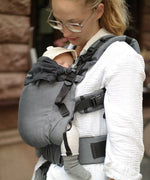Side of mother wearing a Didymos didyfix baby full buckle carrier in double anthracite with a baby sitting inside