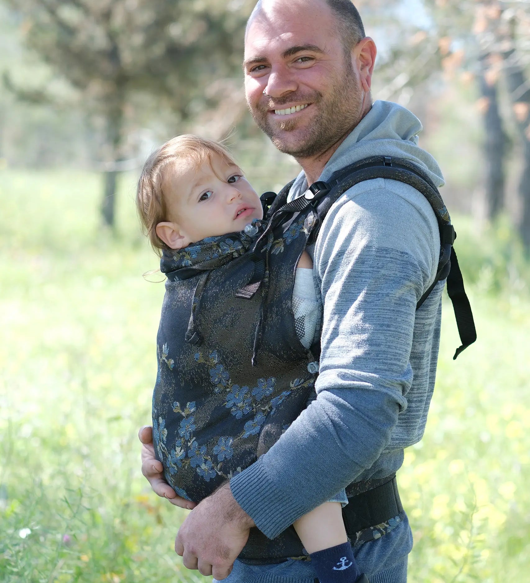 Side of father carrying a toddler in the blue blossom Didymos didyfix toddler carrier in the frontal position with the neck rest adjusted to the head