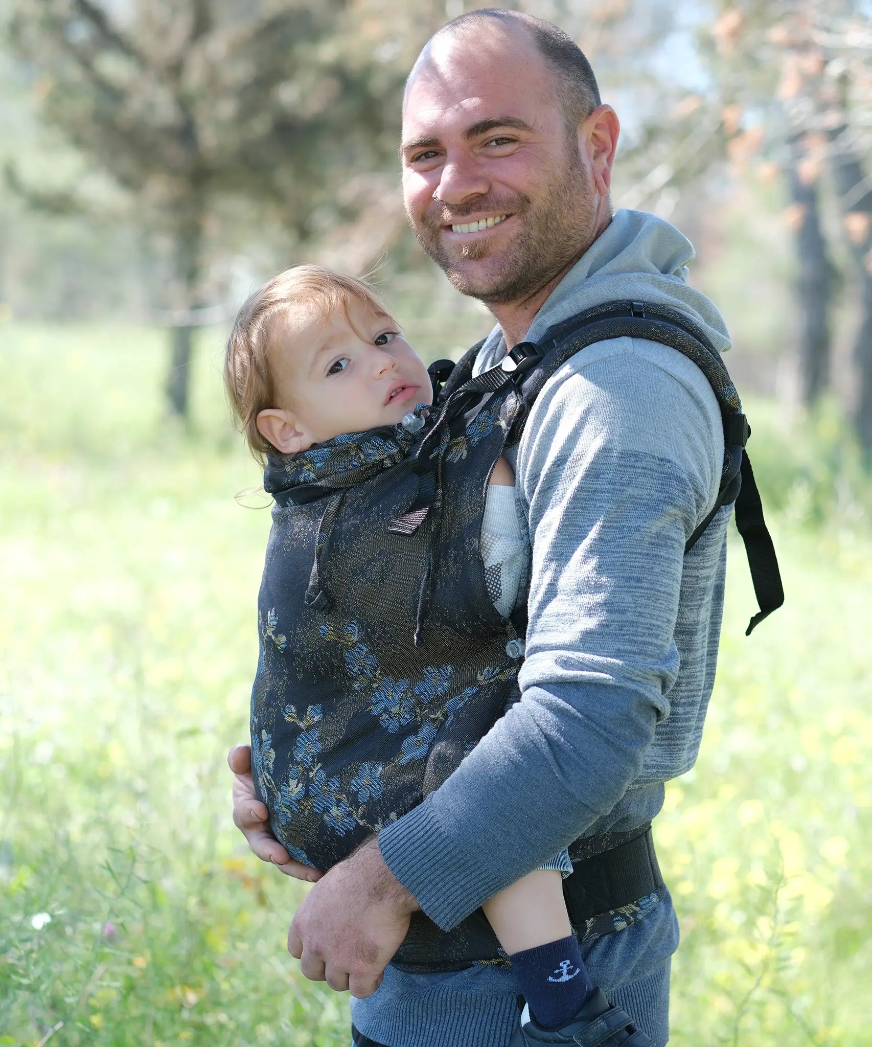 Side of father carrying a toddler in the blue blossom Didymos didyfix toddler carrier in the frontal position with the neck rest adjusted to the head