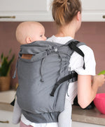 Woman carrying a small child on the back with a Didymos didyfix double anthracite toddler carrier showing neck rest adjusted to baby's head position