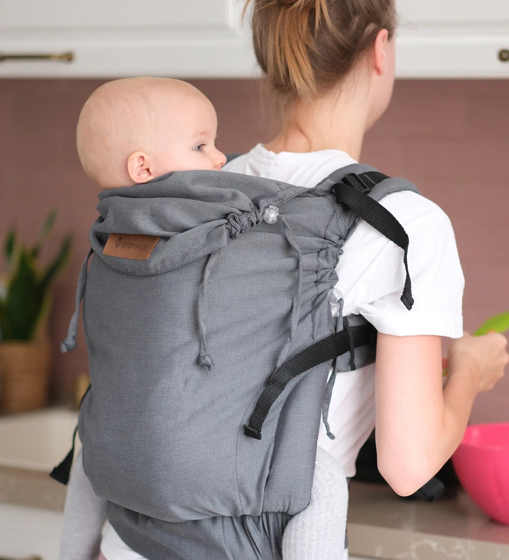 Woman carrying a small child on the back with a Didymos didyfix double anthracite toddler carrier showing neck rest adjusted to baby's head position