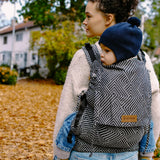 Mother carrying a small child on the back with a Didymos didyfix full buckle metro monochrom toddler carrier made from cotton