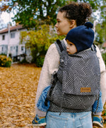 Mother carrying a small child on the back with a Didymos didyfix full buckle metro monochrom toddler carrier made from cotton