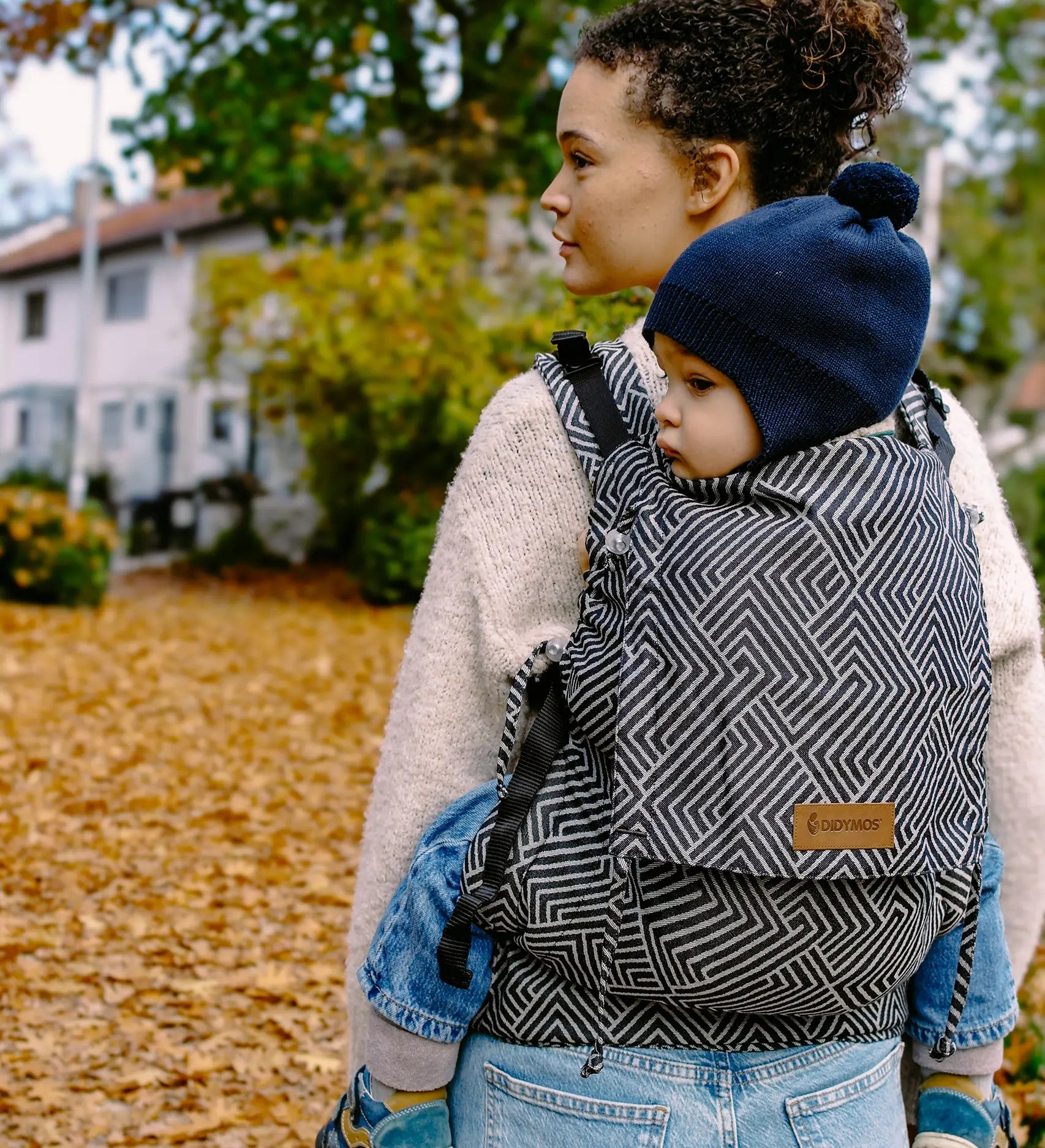 Mother carrying a small child on the back with a Didymos didyfix full buckle metro monochrom toddler carrier made from cotton
