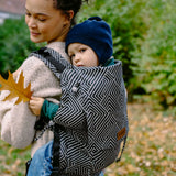 Toddler sitting inside a Didiymos didyfix toddler carrier in metro monochrome carried on a mother's back 