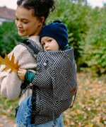 Toddler sitting inside a Didiymos didyfix toddler carrier in metro monochrome carried on a mother's back 