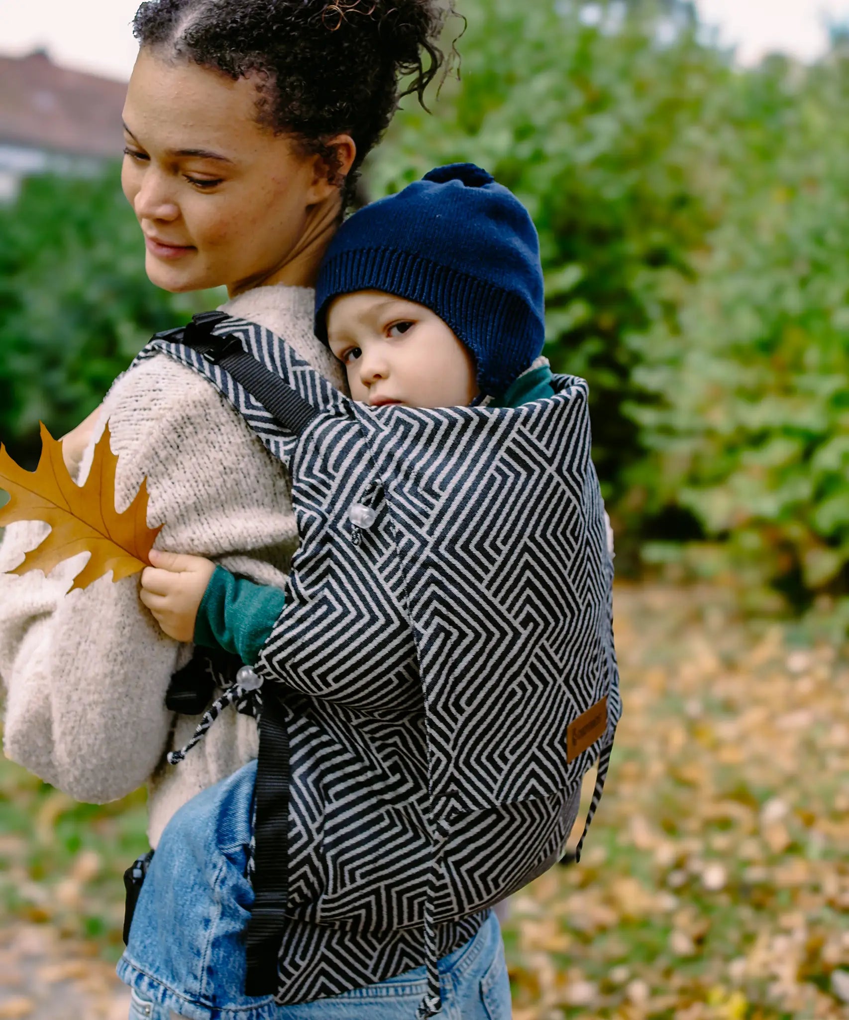 Toddler sitting inside a Didiymos didyfix toddler carrier in metro monochrome carried on a mother's back 