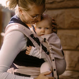 Side of Mother carrying a baby in a cinnamon Didymos didyflow half buckle cotton carrier in the frontal position 