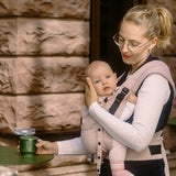 Mother carrying a baby in a cinnamon Didymos didyflow half buckle half tie carrier with the neck rest adjusted to baby's head position.