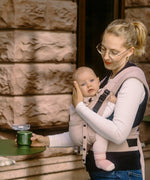 Mother carrying a baby in a cinnamon Didymos didyflow half buckle half tie carrier with the neck rest adjusted to baby's head position.
