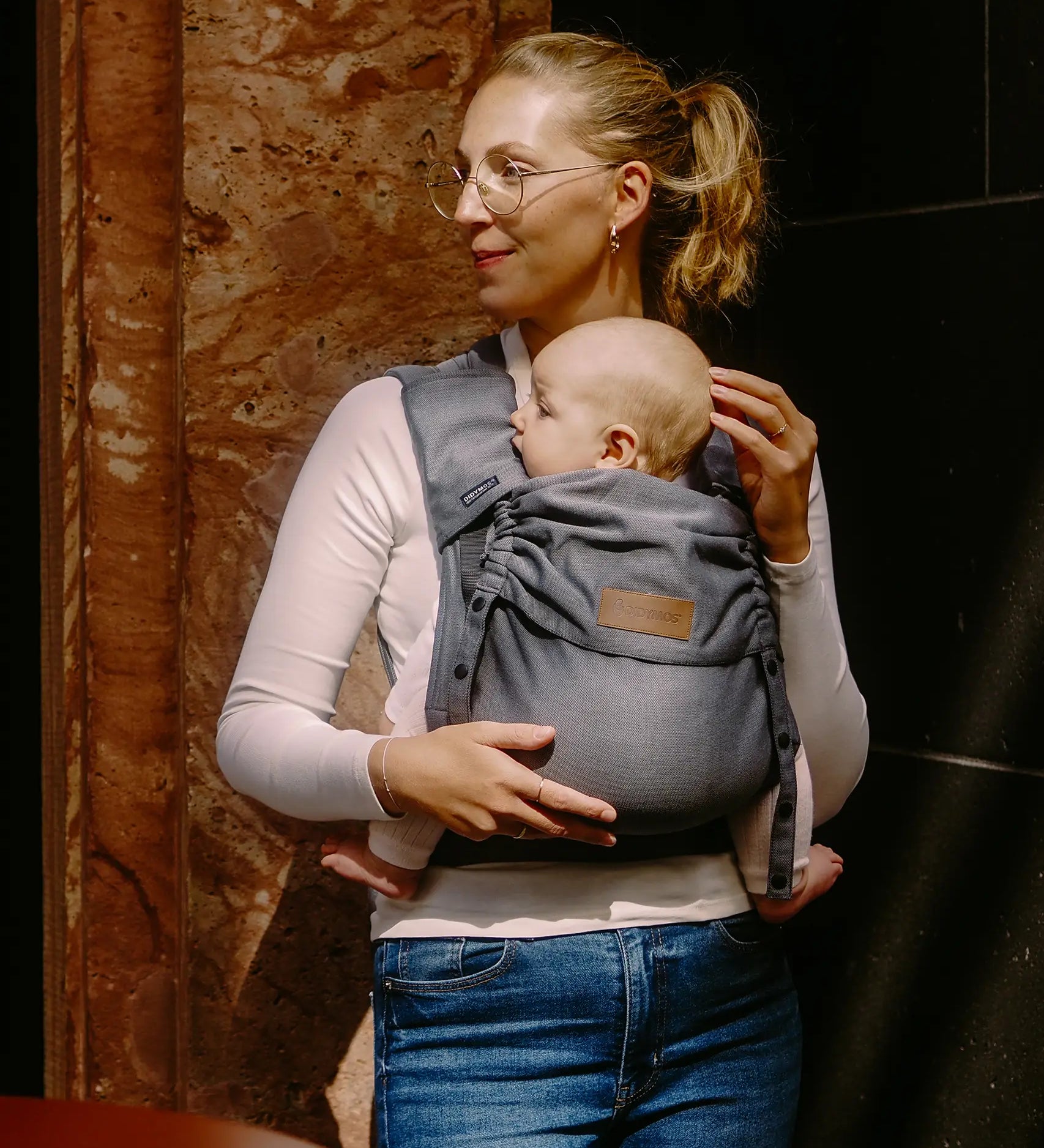 Mother carrying a baby in a Didymos didyflow half buckle half tie cotton carrier in the frontal position in double anthracite 