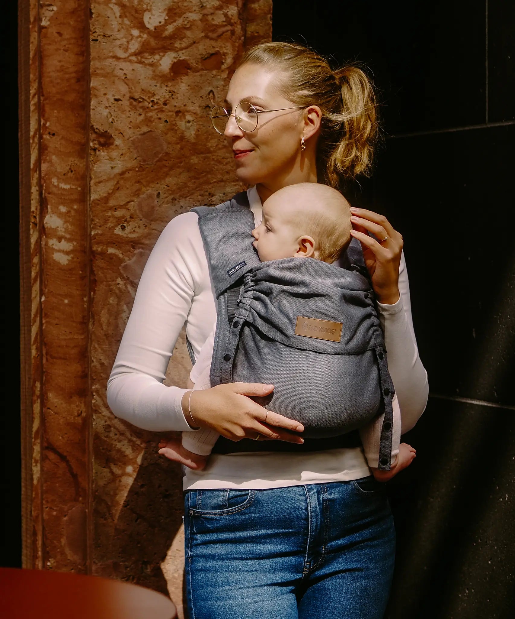 Mother carrying a baby in a Didymos didyflow half buckle half tie cotton carrier in the frontal position in double anthracite 