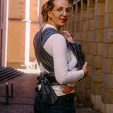 Back of mother wearing a Didymos didyflow double anthracite baby carrier showing half buckle half tie waist belt and double layered tie on shoulder straps