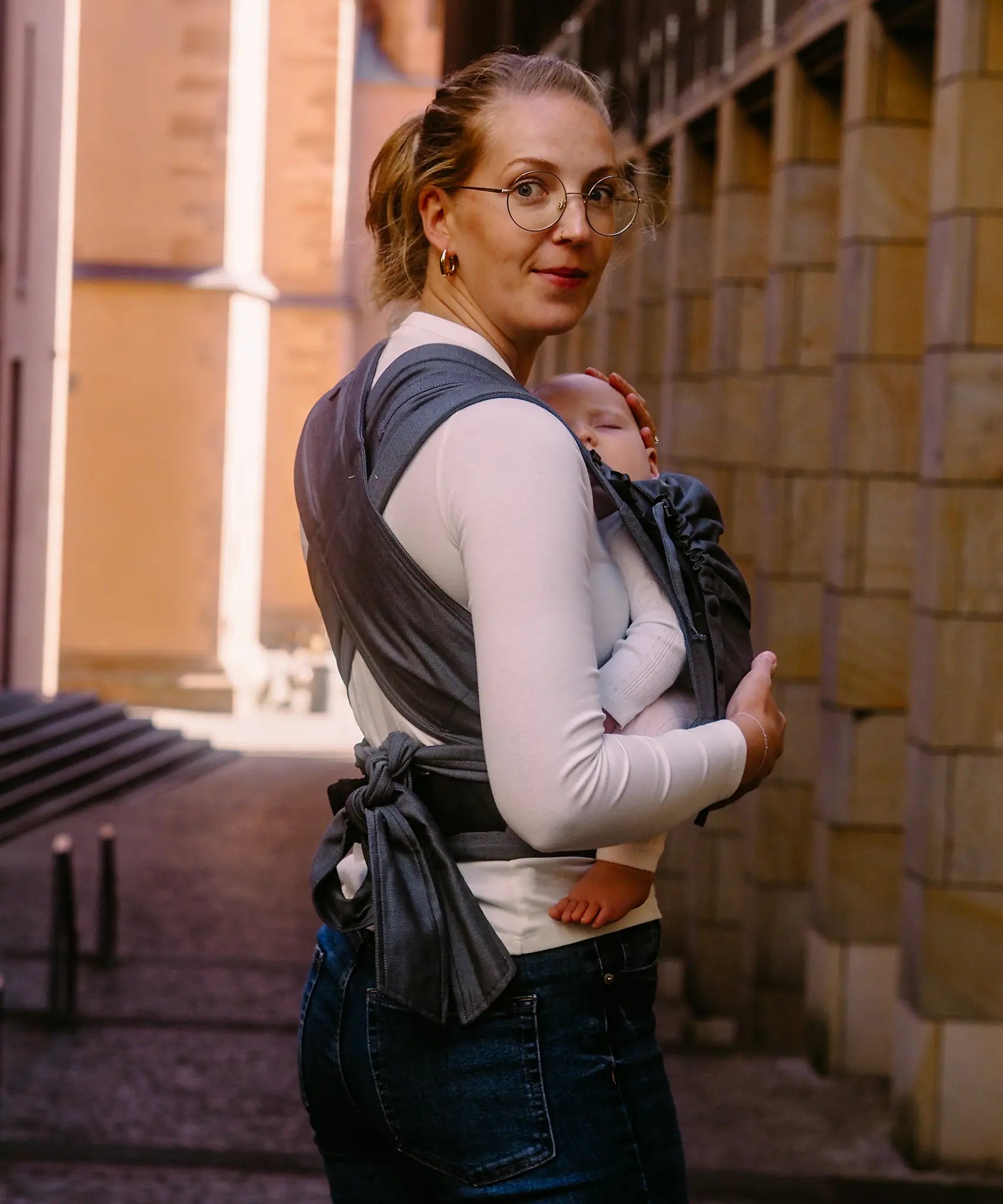 Back of mother wearing a Didymos didyflow double anthracite baby carrier showing half buckle half tie waist belt and double layered tie on shoulder straps