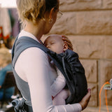 Side of Mother carrying a baby in a double anthractie Didymos didyflow half buckle half tie cotton carrier in the frontal position 