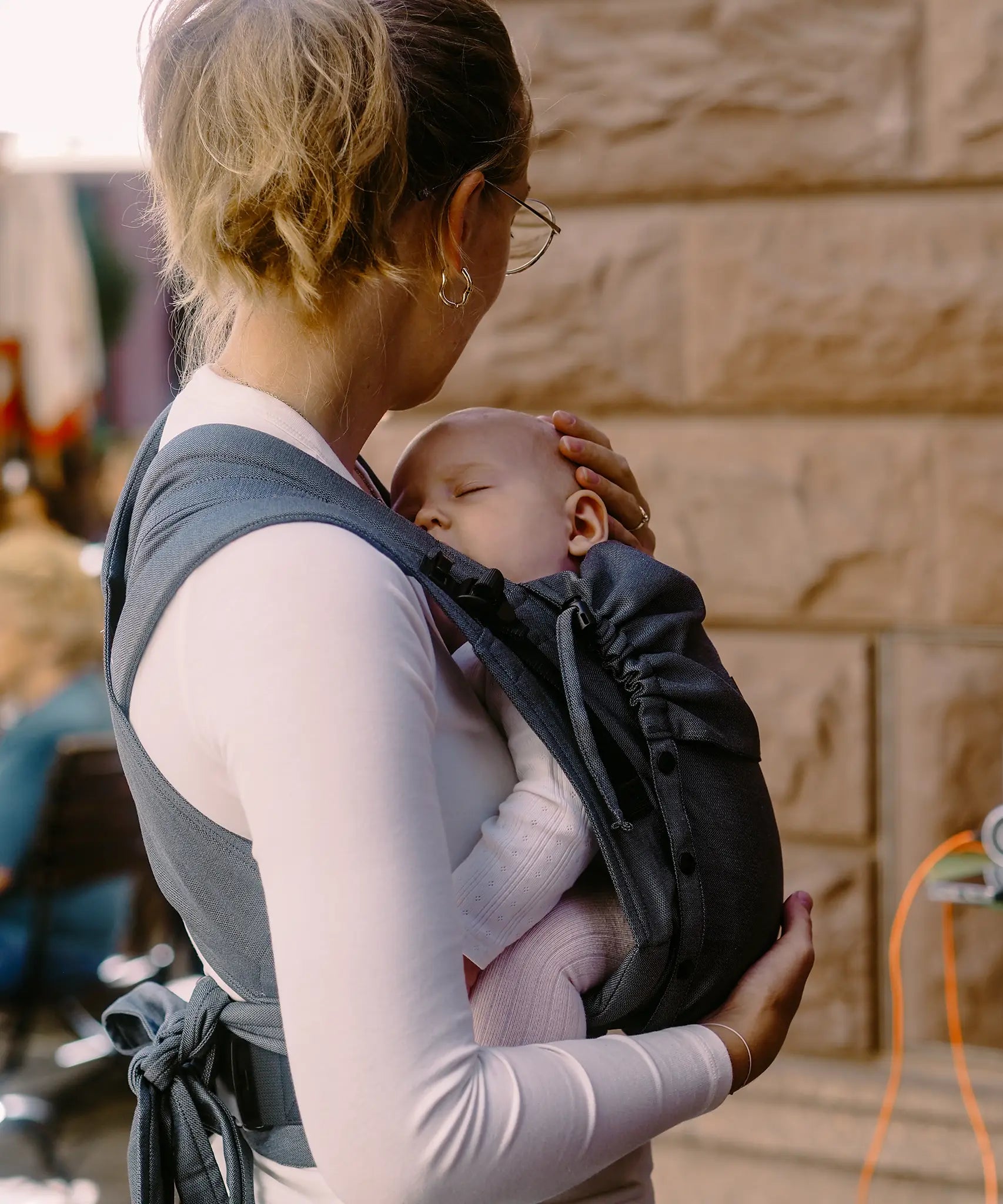 Side of Mother carrying a baby in a double anthractie Didymos didyflow half buckle half tie cotton carrier in the frontal position 