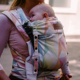 Mother carrying a baby in the zephyr  Didymos didyflow half buckle carrier in the frontal postion showing neck rest adjusted to baby's head position. 