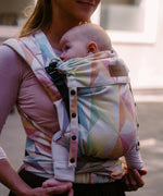 Mother carrying a baby in the zephyr  Didymos didyflow half buckle carrier in the frontal postion showing neck rest adjusted to baby's head position. 