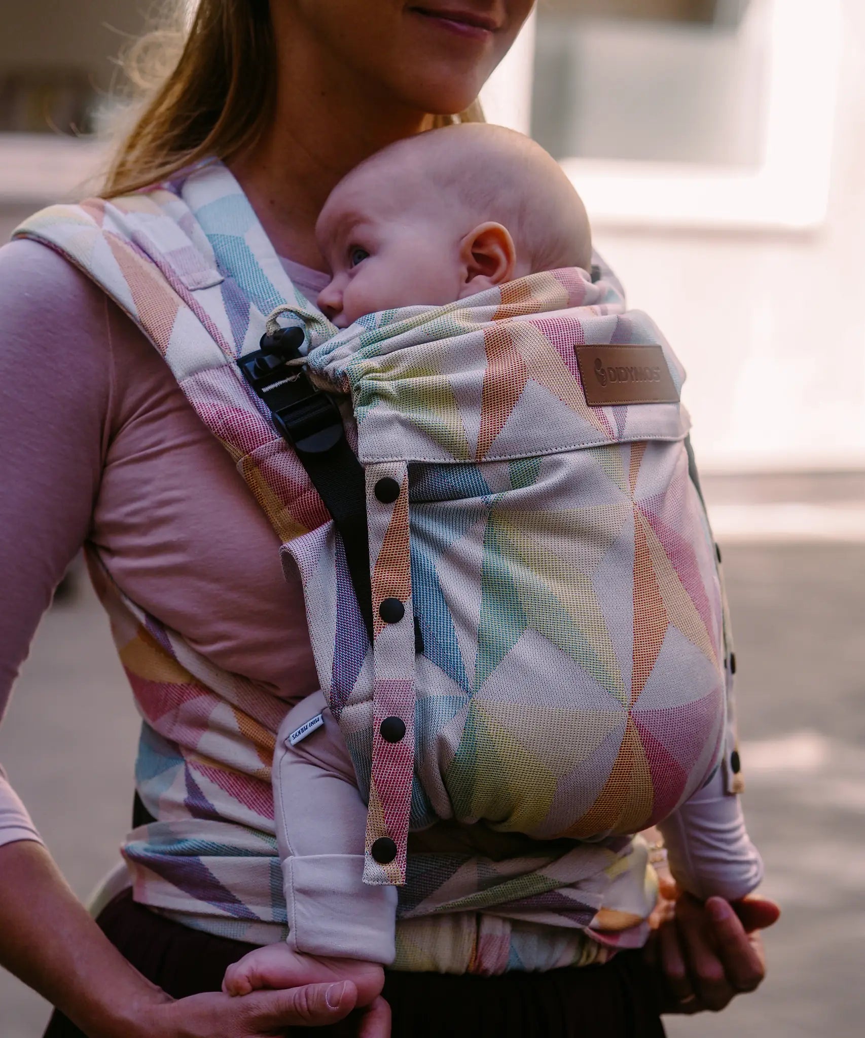 Mother carrying a baby in the zephyr  Didymos didyflow half buckle carrier in the frontal postion showing neck rest adjusted to baby's head position. 