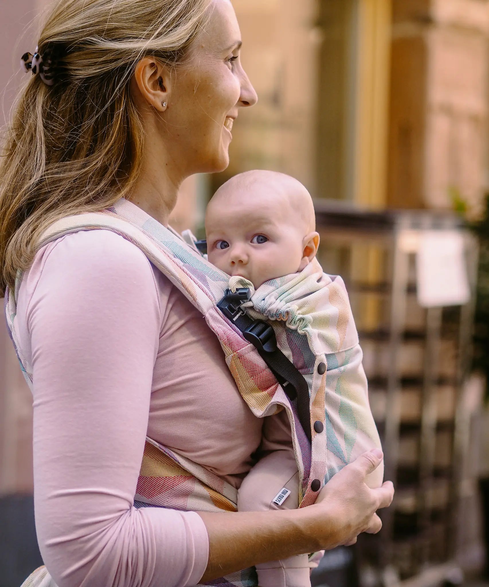 Side of mother carrying a baby in the zephyr Didymos didyflow half buckle half tie carrier in the frontal position showing neck/head rest detail