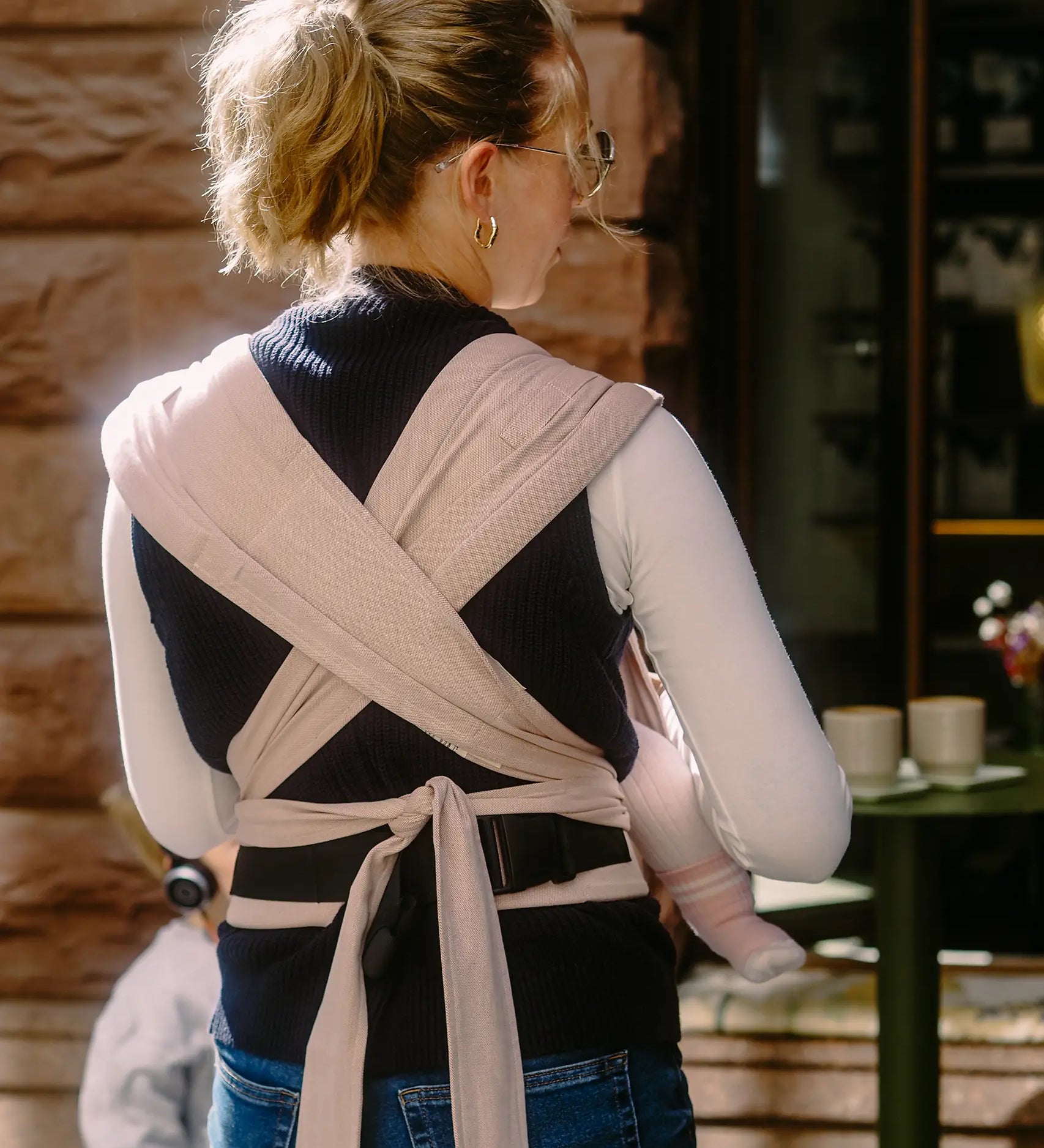 Back of mother wearing a Didymos didyflow cinnamon carrier showing half buckle half tie waist belt and double layered tie on shoulder straps