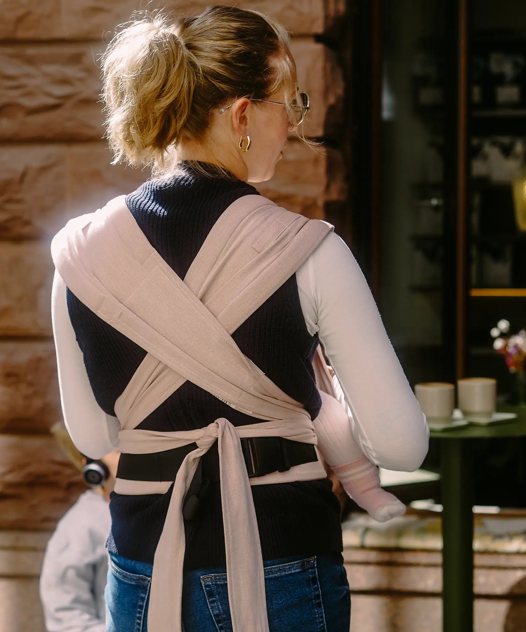 Back of mother wearing a Didymos didyflow cinnamon carrier showing half buckle half tie waist belt and double layered tie on shoulder straps