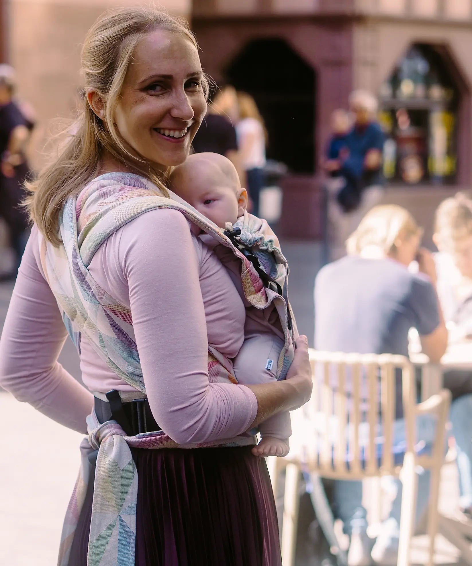 Back of mother wearing a Didymos didyflow zephyr baby carrier showing half buckle half tie waist belt and double layered tie on shoulder straps
