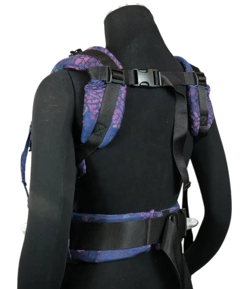 Back of a Didymos didyfix baby carrier in mosaic in the dark shown on mannequin. showing padded shoulder straps and buckle fasteners