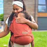 Mother carrying a baby in the frontal position in the Didymos didyfix full buckle toddler carrier in rusty red