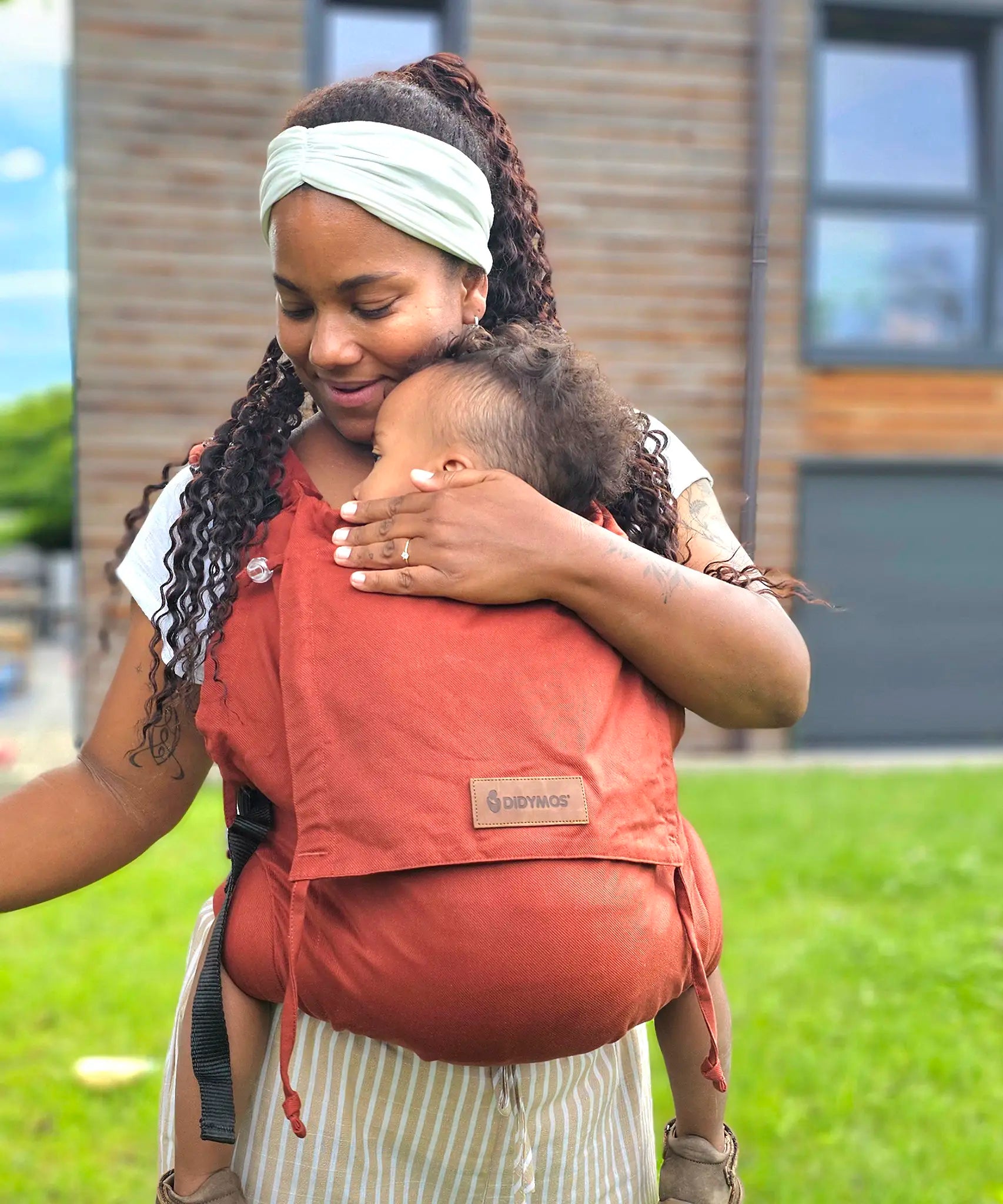Mother carrying a baby in the frontal position in the Didymos didyfix full buckle toddler carrier in rusty red
