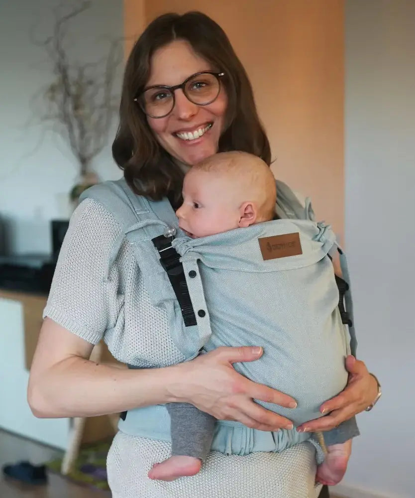 Mother carrying a baby in a Didymos didyflow half buckle  half tie carrier in the frontal position in ocean blue