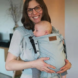 Mother carrying a baby in a Didymos didyflow half buckle  half tie carrier in the frontal position in ocean blue