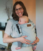 Mother carrying a baby in a Didymos didyflow half buckle  half tie carrier in the frontal position in ocean blue