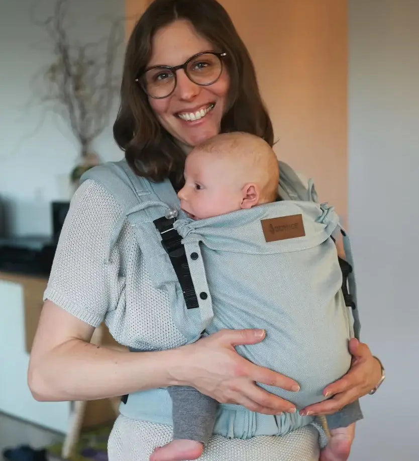 Mother carrying a baby in a Didymos didyflow half buckle  half tie carrier in the frontal position in ocean blue